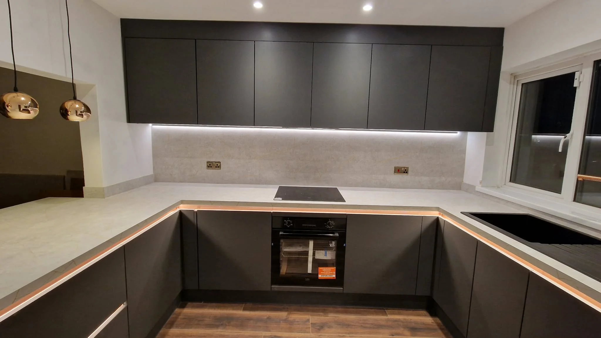 Modern kitchen fitting with dark cabinetry, worktops and integrated lighting